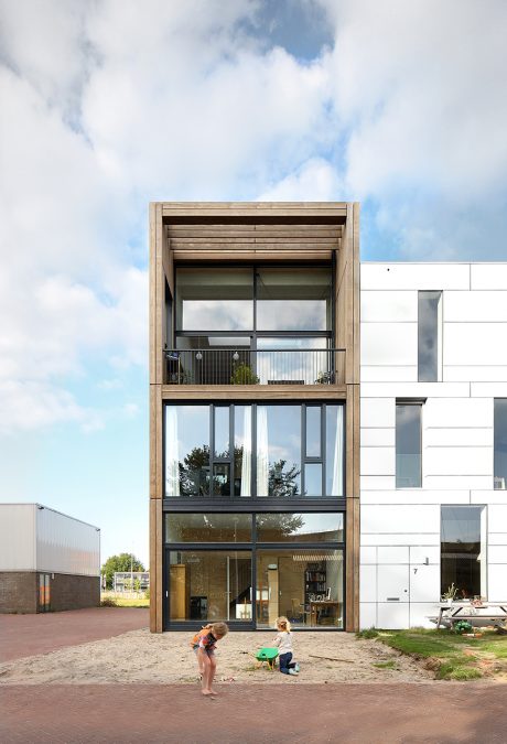 A modern, multi-story building with a wooden facade and large glass windows showcasing the interior.