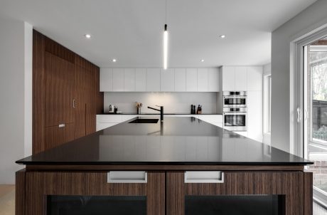 Sleek, minimalist kitchen design with dark wood cabinetry, white walls, and a large central island with a black countertop.