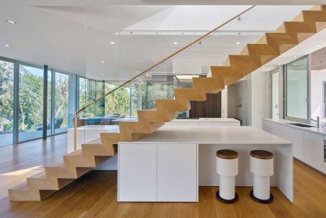 Striking modern interior with sleek wooden staircase, minimalist furnishings, and floor-to-ceiling windows.