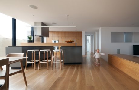 Sleek kitchen with wood cabinetry, island, and modern stools; open-concept living space.