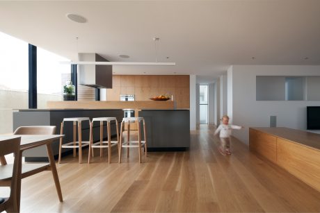 Sleek kitchen with wood cabinetry, island, and modern stools; open-concept living space.