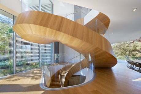 Striking spiral staircase with curved wooden treads and glass balustrade in modern interior.