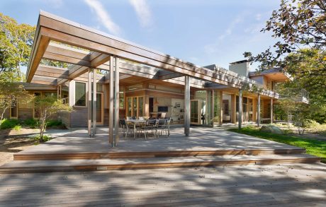 Modern, wood-framed exterior with large glass doors, sheltered patio, and lush garden surroundings.