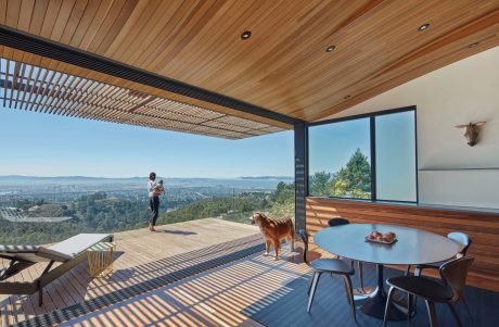 A modern, open-plan living space with a breathtaking panoramic view, wood-paneled ceiling, and outdoor deck.