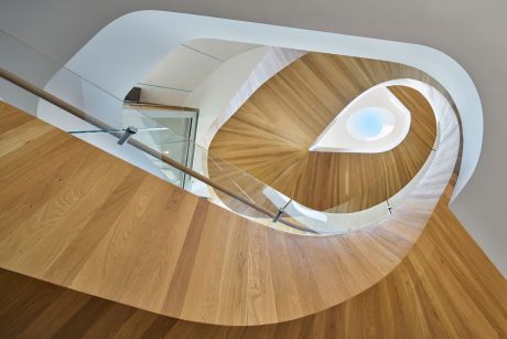 Curved, spiraling staircase with wooden steps and glass balustrades in modern interior.