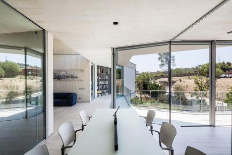 Sleek, minimalist interior with expansive glass walls and a long wooden table overlooking lush vegetation.