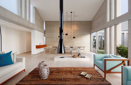 A modern, minimalist living room with concrete walls, wooden furniture, and a striking black fireplace.