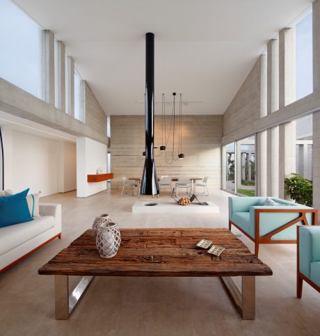 A modern, minimalist living room with concrete walls, wooden furniture, and a striking black fireplace.