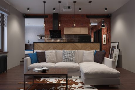 A modern, cozy living room with exposed brick walls, wooden kitchen cabinets, and a plush sectional sofa.