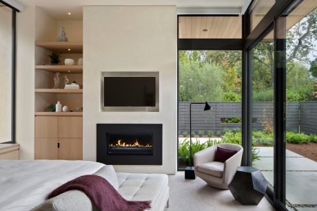 Modern bedroom with fireplace, built-in shelving, and panoramic outdoor views.
