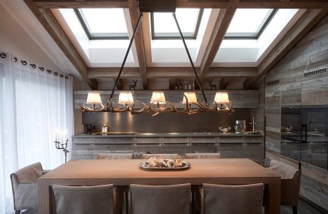 Rustic wood beams, antler chandeliers, and skylit kitchen in cozy chalet design.