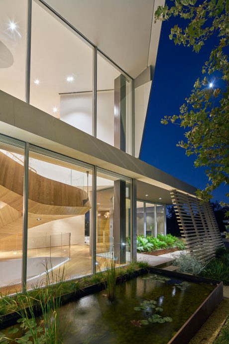 Sleek, modern architecture with extensive glass walls, wooden accents, and water feature.