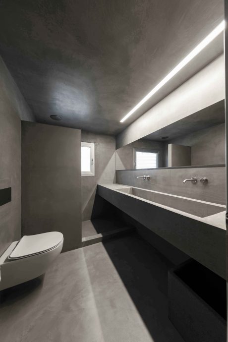 A modern, minimalist bathroom with a concrete vanity and recessed lighting fixtures.