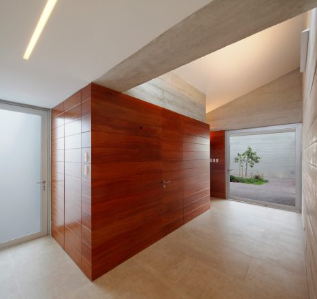 Spacious entryway with concrete walls, wood paneling, and a large window overlooking greenery.
