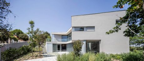 Modern architectural exterior with sleek lines, large windows, and lush greenery surrounding the building.