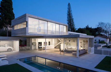 Contemporary two-story house with glass walls, swimming pool, and lush landscaping.