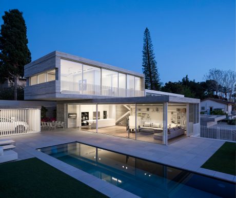 Contemporary two-story house with glass walls, swimming pool, and lush landscaping.