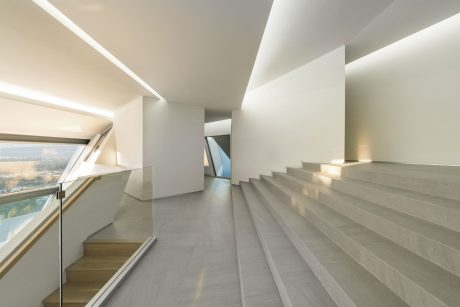 A modern, minimalist interior with sleek stairs, clean lines, and large windows offering a scenic view.