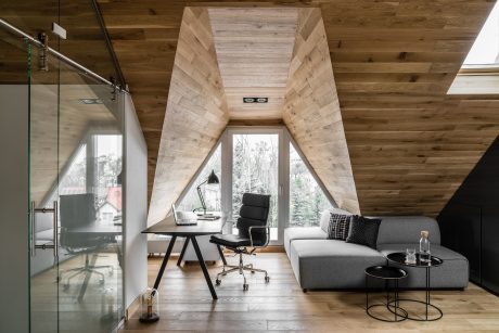 Rustic A-frame cabin interior with modern furniture, large windows, and wooden walls.