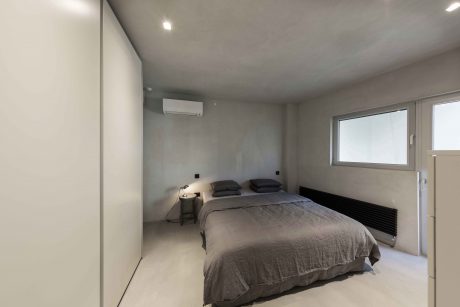 Modern, minimalist bedroom with sleek, white walls, hardwood flooring, and accent lighting.
