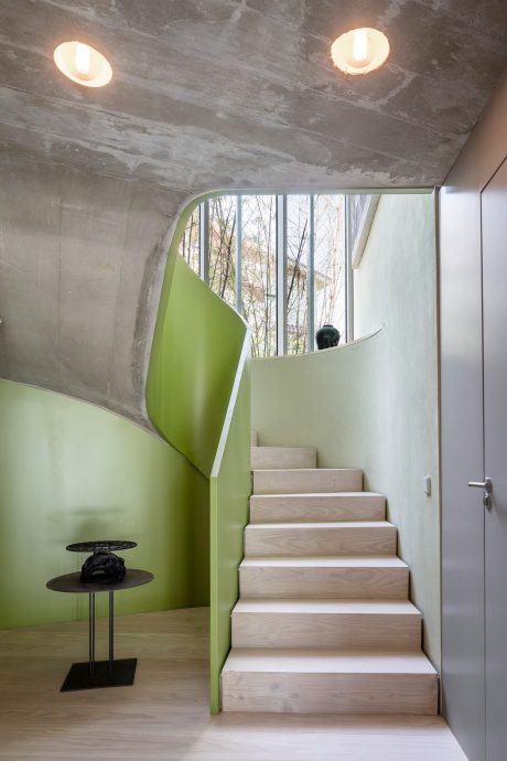 A modern, minimalist staircase with a striking green accent wall and large windows.