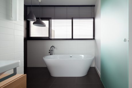 A modern bathroom with a freestanding bathtub, black window blinds, and minimalist lighting.