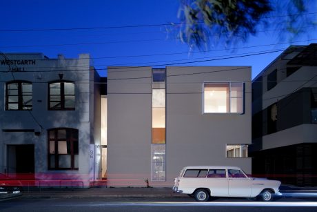 A modern multi-story building with clean lines and large windows, parked vintage car in foreground.