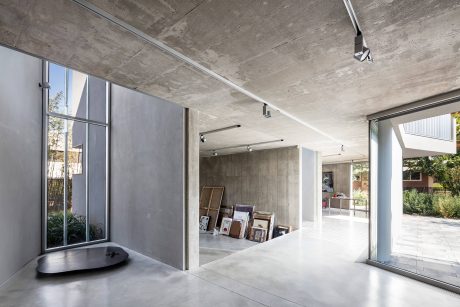 Minimalist interior with exposed concrete walls and ceiling, track lighting, and large glass windows.