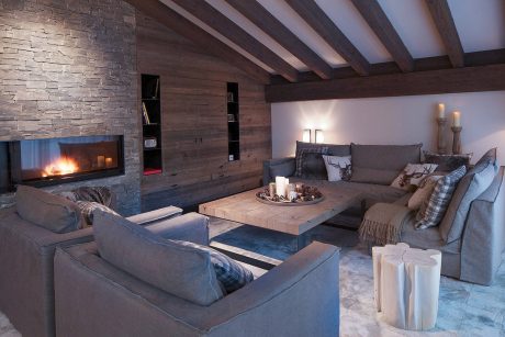 A cozy, rustic-style living room with a stone fireplace, wooden beams, and a large, inviting sofa arrangement.