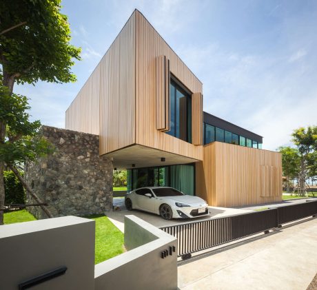 A modern, wooden-clad house with a striking geometric design, nestled in a lush green setting.