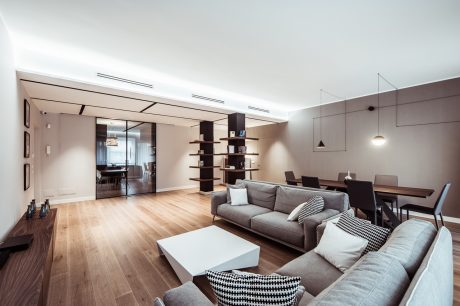 Spacious, minimalist living room with wooden floors, modern furniture, and recessed lighting.