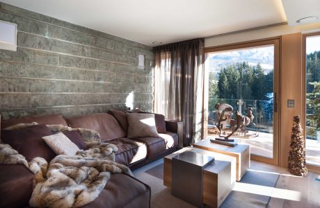 A cozy living room with brown leather sofas, wooden accents, and large windows overlooking nature.