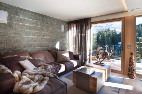 A cozy living room with brown leather sofas, wooden accents, and large windows overlooking nature.