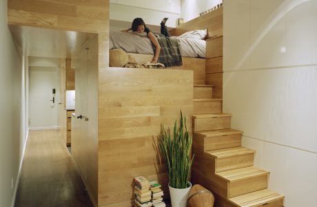 A cozy, minimalist loft space with a wooden staircase and elevated sleeping area.