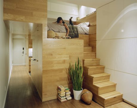 A cozy, minimalist loft space with a wooden staircase and elevated sleeping area.