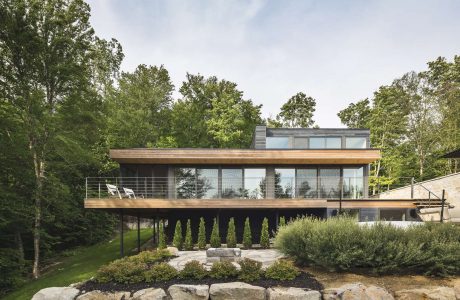 Modern two-story home with large windows, wooden accents, and lush landscaping.