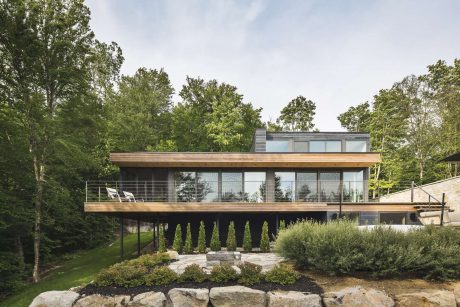 Modern two-story home with large windows, wooden accents, and lush landscaping.