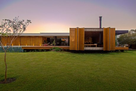 A modern, wooden structure with open spaces, surrounded by a lush, grassy lawn. Architectural details highlight natural materials and design.