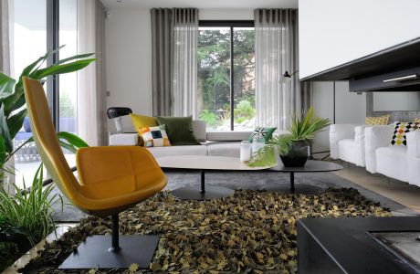 A modern, minimalist living room with a yellow armchair, potted plants, and a large window.