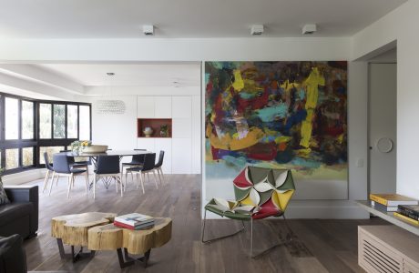 A modern, open-concept living space with a vibrant abstract painting, colorful furniture, and natural wood accents.