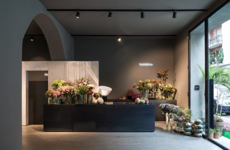 Modern floral shop interior with sleek black counter, arched alcove, track lighting.