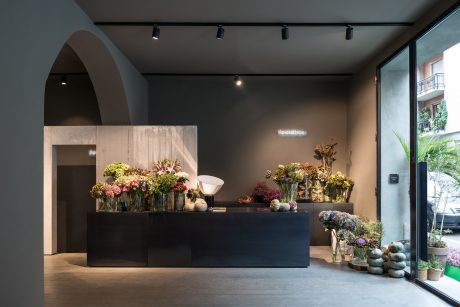 Modern floral shop interior with sleek black counter, arched alcove, track lighting.