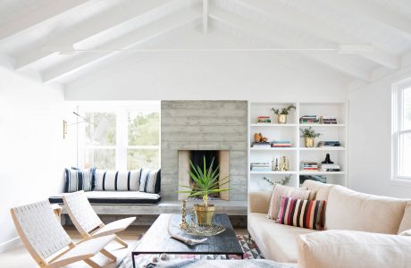 Bright, open-concept living room with high ceilings, stone fireplace, and built-in shelving.