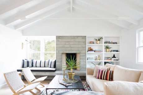 Bright, open-concept living room with high ceilings, stone fireplace, and built-in shelving.