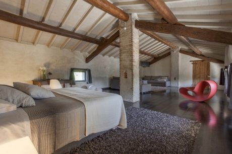 Rustic attic bedroom with exposed wooden beams, plush furnishings, and unique red chair.