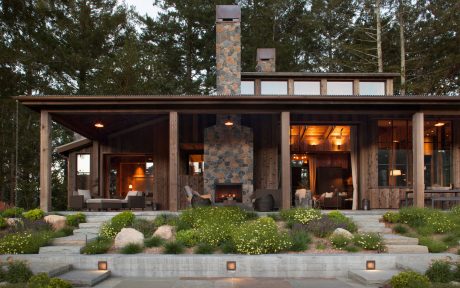 Rustic lodge-style home with stone fireplace, covered porch, and landscaped grounds.