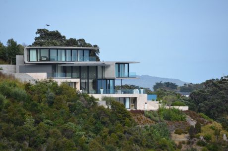 Modern, multi-level beachside residence with glass walls, terraces, and lush landscaping.