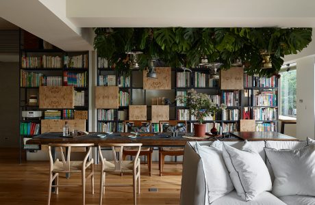 Cozy home library with floor-to-ceiling bookshelves, tropical plants, and a wooden dining table.