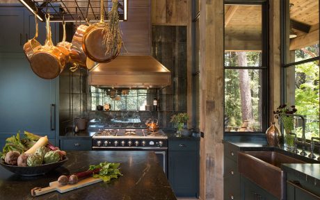 Rustic, cozy kitchen with dark cabinets, copper pots, and large window overlooking nature.