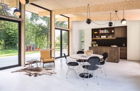 A modern, open-concept living space with wooden beams, black furniture, and large windows.